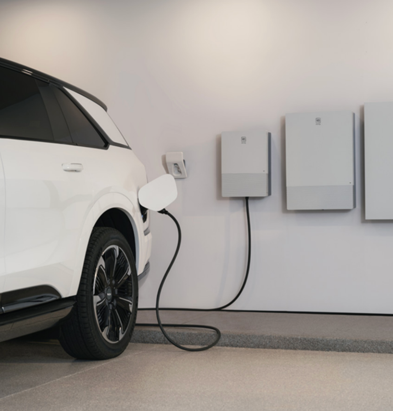 Un coche eléctrico blanco se está recargando en una toma de corriente de pared, con dos baterías grandes debajo.