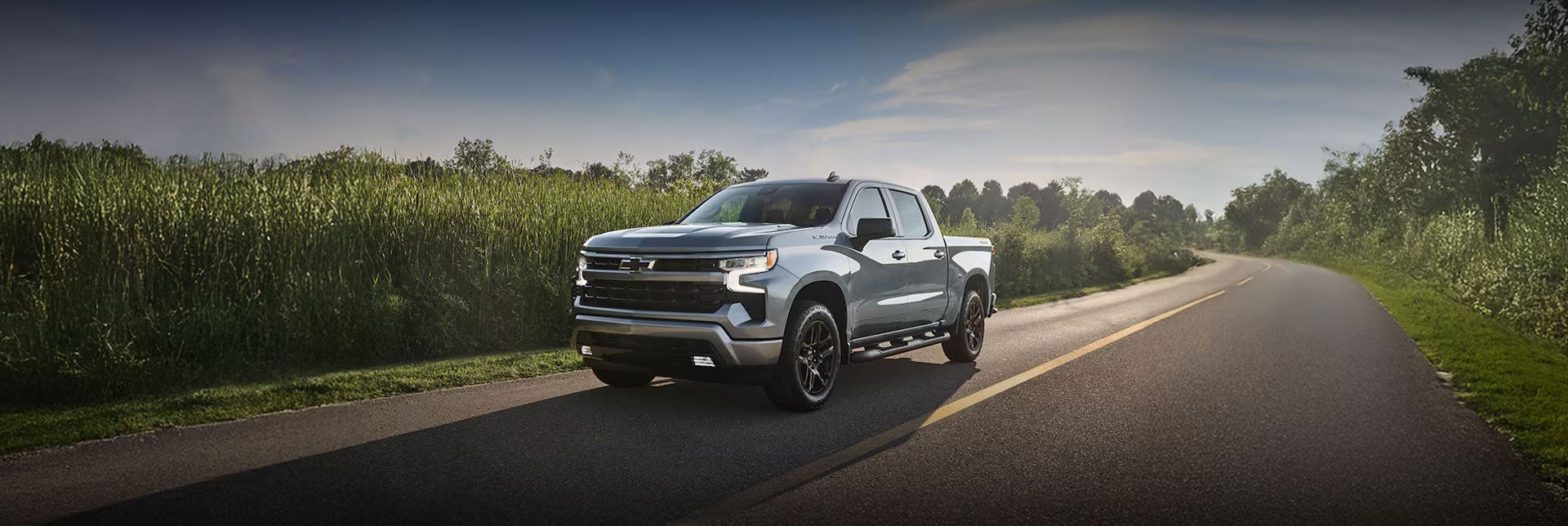Vista de tres cuartos de una Chevy Silverado 1500 circulando por una carretera bordeada de vegetación, con un texto superpuesto que dice: «¿No puedes esperar?».
